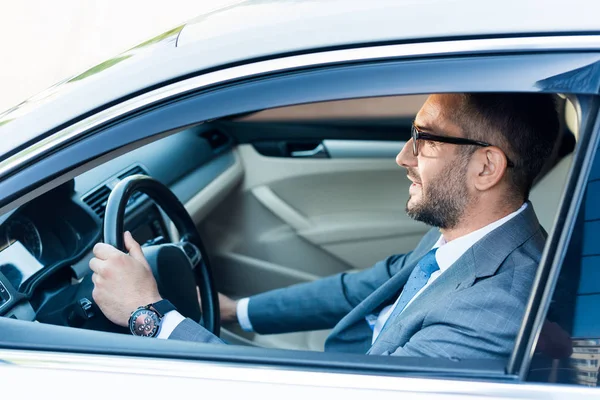 Seitenansicht eines Geschäftsmannes in Anzug und Brille, der allein Auto fährt — Stockfoto