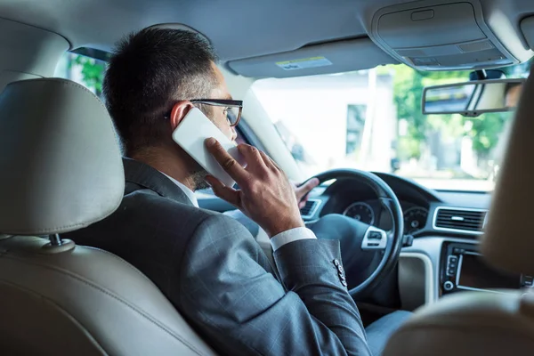 Rückansicht eines Geschäftsmannes, der während der Autofahrt mit dem Smartphone spricht — Stockfoto