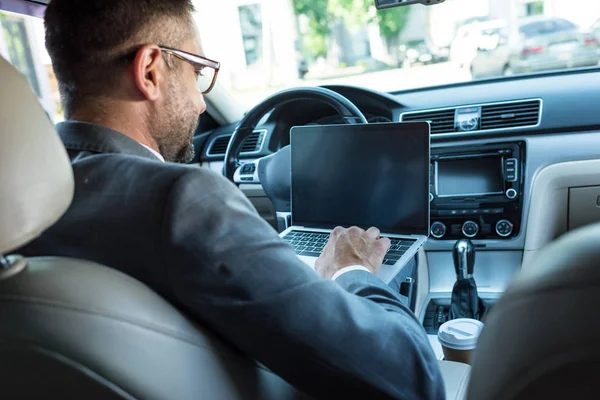 Back view of businessman in eyeglasses using laptop with blank screen in car — Stock Photo