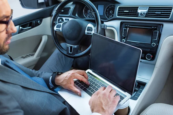 Uomo d'affari in occhiali da vista utilizzando laptop con schermo vuoto in auto — Foto stock