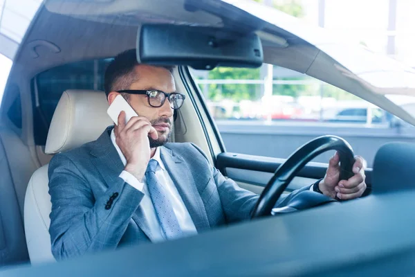 Seitenansicht eines Geschäftsmannes, der während der Autofahrt auf dem Smartphone spricht — Stockfoto