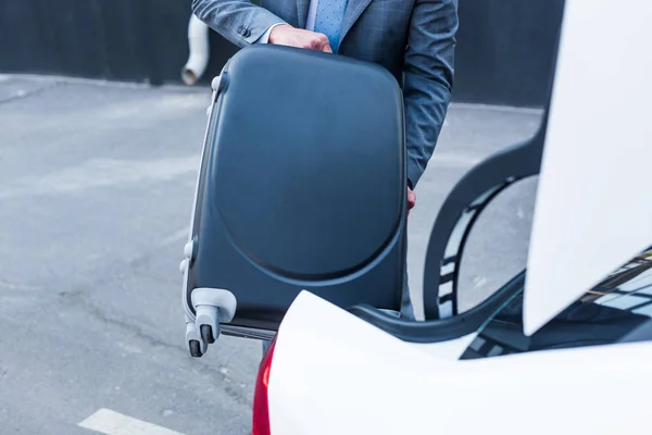 Cropped shot of businessman putting luggage into car on parking — Stock Photo