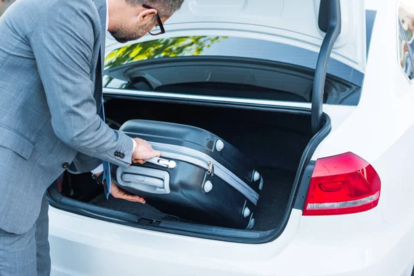 Частичный взгляд бизнесмена, кладущего багаж в машину на парковке — стоковое фото