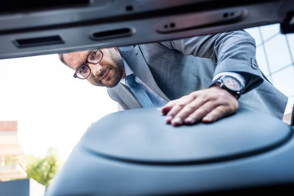 Selektiver Fokus des Geschäftsmannes mit Brille, der sein Gepäck auf dem Parkplatz ins Auto legt — Stockfoto