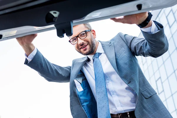 Бизнесмен в костюмах и очках заглядывает в багажник автомобиля — стоковое фото
