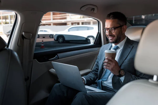 Усміхаючись бізнесмен в окулярів з кави до йти за допомогою ноутбука на верх в автомобілі — стокове фото