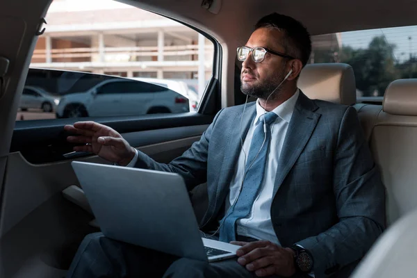 Homem de negócios em fones de ouvido com laptop ouvindo música no carro — Fotografia de Stock