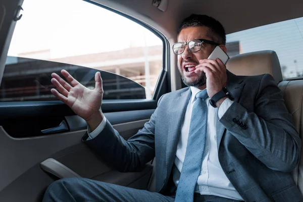 Empresario emocional hablando en el teléfono inteligente mientras está sentado en el asiento trasero en el coche - foto de stock