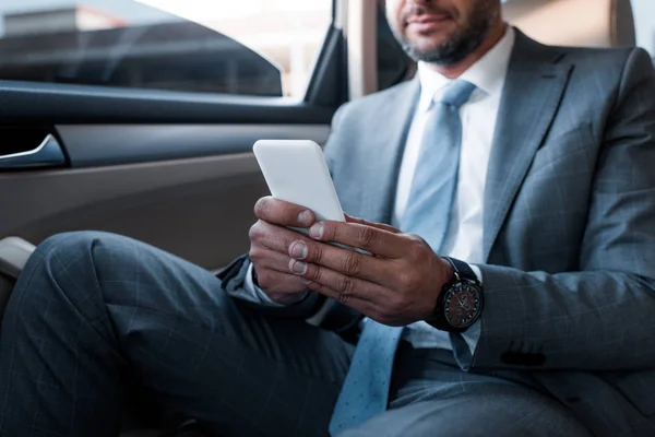 Partial view of businessman using smartphone while sitting on backseat in car — Stock Photo