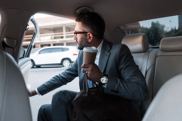 Uomo d'affari con caffè per andare seduto in macchina con porta aperta — Foto stock