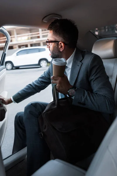 Homme d'affaires avec café pour aller assis dans la voiture avec porte ouverte — Photo de stock