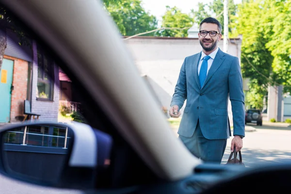 Hombre de negocios en traje y gafas con llaves de coche va a coche en la calle - foto de stock