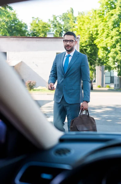 Uomo d'affari in giacca e cravatta e occhiali con le chiavi della macchina che vanno in macchina per strada — Foto stock
