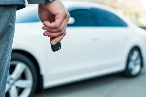 Vista parcial del hombre de negocios con las llaves del coche en la mano y el coche en el fondo - foto de stock