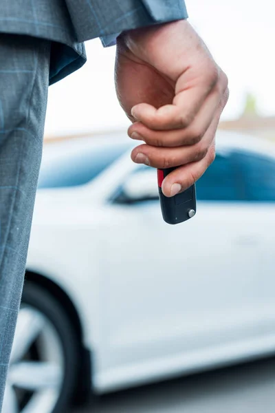 Vista parcial del hombre de negocios con las llaves del coche en la mano y el coche en el fondo - foto de stock
