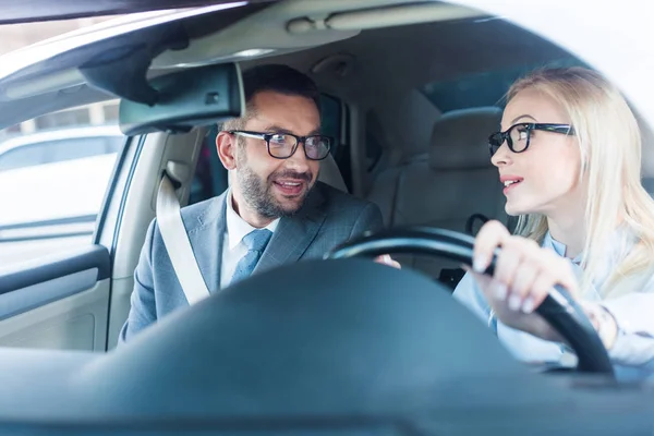 Portrait d'une femme d'affaires blonde à lunettes conduisant une voiture avec un collègue proche — Photo de stock