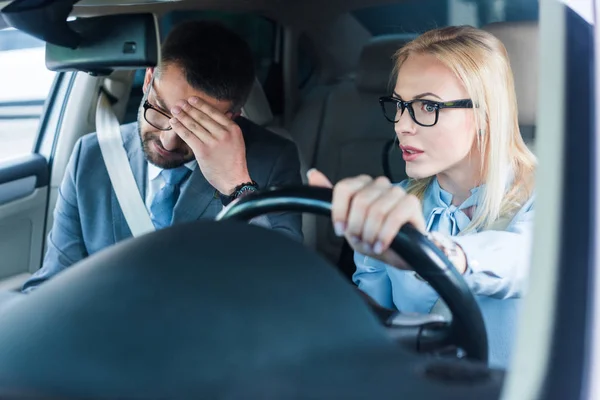 Портрет блондинки-предпринимательницы в очках за рулем автомобиля с коллегой рядом — стоковое фото