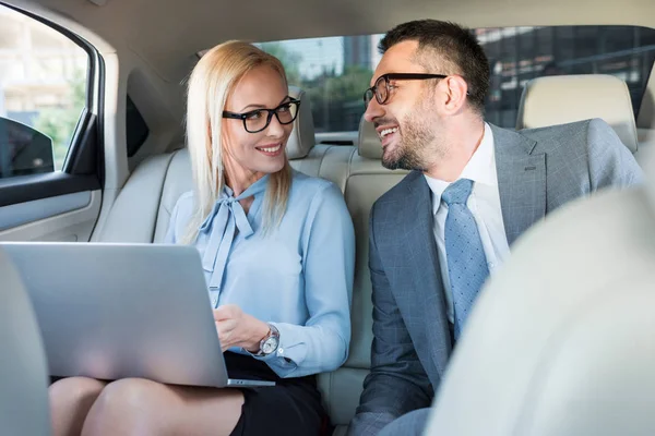 Portrait of smiling business people with laptop on back seats in car — Stock Photo