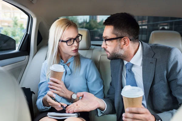 Retrato de empresários com café para ir discutir o trabalho em assentos traseiros no carro — Fotografia de Stock