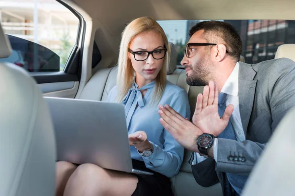 Ritratto di uomini d'affari con computer portatile che discutono il lavoro sui sedili posteriori in auto — Foto stock