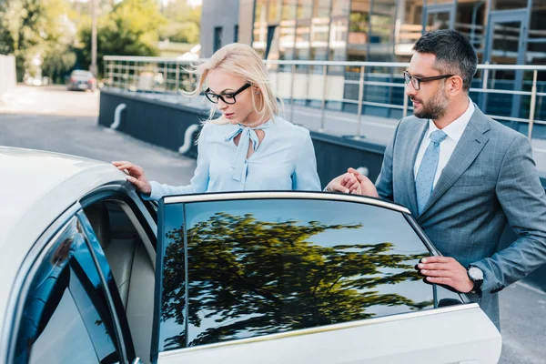 Portrait of businessman helping colleague sit into car on street — Stock Photo