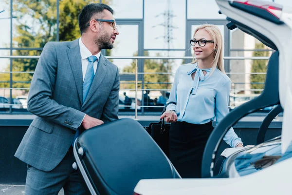 Retrato del hombre de negocios poniendo equipaje en el coche con su colega cerca de - foto de stock