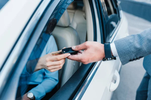 Tiro cortado de empresário dando chaves de carro para colega no assento do motorista no carro — Fotografia de Stock