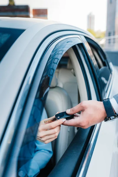 Cropped shot of businessman giving car keys to colleague at driver seat in car — Stock Photo