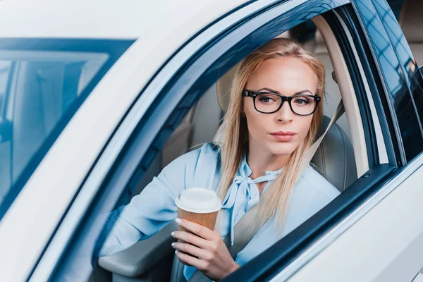 Portrait of blonde businesswoman with coffee to go driving car — Stock Photo