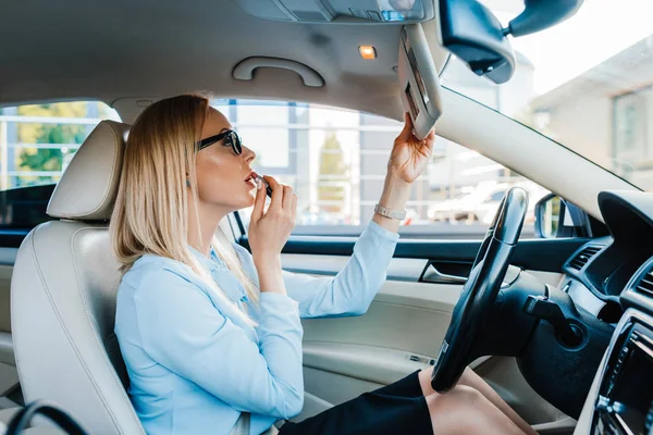 Seitenansicht der attraktiven Geschäftsfrau, die Lippenstift im Auto aufträgt — Stockfoto