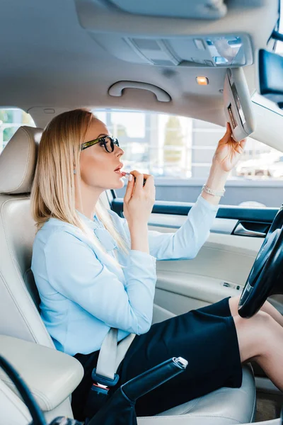 Seitenansicht der attraktiven Geschäftsfrau, die Lippenstift im Auto aufträgt — Stockfoto