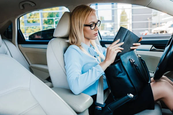 Vue latérale de la femme d'affaires dans les lunettes vérifier portefeuille dans la voiture — Photo de stock