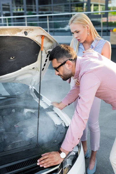 Side view of couple looking under car hood of broken car on street — Stock Photo