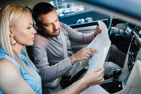 Vista lateral de pareja en busca de destino en el mapa mientras está sentado en el coche - foto de stock