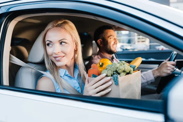 Messa a fuoco selettiva di coppia sposata con sacchetto di carta pieno di cibo sano in auto — Foto stock