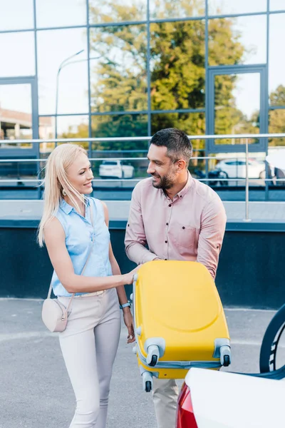 Smiling married couple putting luggage into car on parking — Stock Photo