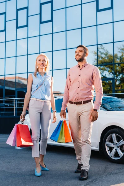 Lächelndes Ehepaar mit Einkaufstüten steht neben Auto auf der Straße — Stockfoto