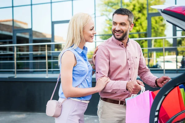 Sonriente pareja casada poniendo bolsas de compras en el coche en la calle - foto de stock