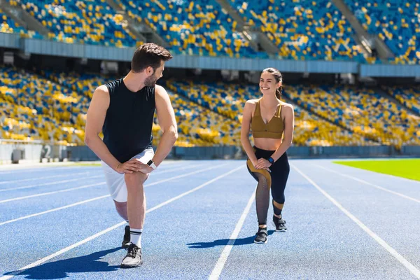Young fit couple warming up legs before jogging on running track at sports stadium — Stock Photo