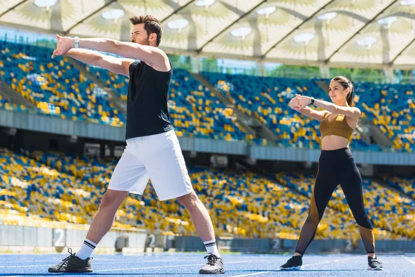 Joven hermosa pareja calentamiento antes de entrenar en pista de atletismo en el estadio deportivo - foto de stock