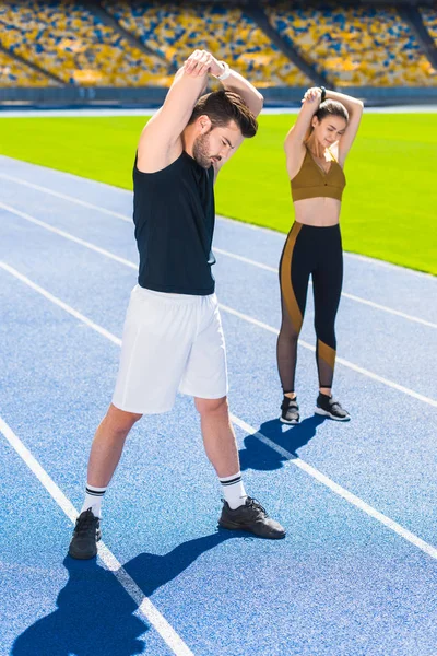 Joven pareja de atletas calentando antes de entrenar en pista de atletismo en el estadio deportivo - foto de stock