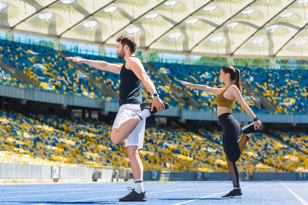 Joven pareja activa calentamiento antes de entrenar en pista de atletismo en el estadio deportivo - foto de stock