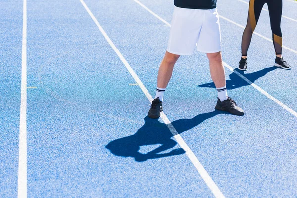Recortado disparo de hombre y mujer en ropa deportiva moderna de pie en pista de atletismo - foto de stock