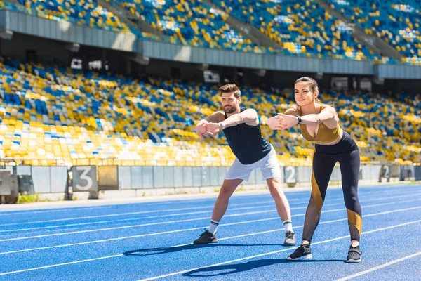 Joven pareja deportiva calentamiento antes de entrenar en pista de atletismo en el estadio deportivo - foto de stock