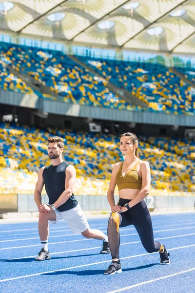 Joven pareja atlética calentándose antes de entrenar en pista de atletismo en el estadio deportivo - foto de stock