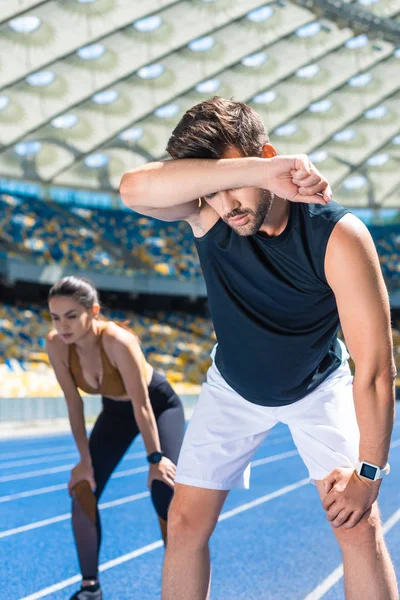 Young exhausted couple standing on running track at sports stadium after jogging — Stock Photo