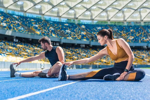 Молодые спортсмены мужского и женского пола бегают на беговой дорожке и растягиваются на спортивном стадионе — стоковое фото