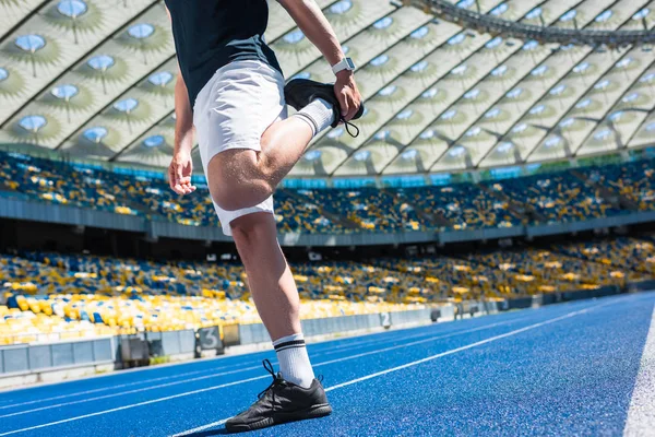 Обрезанный снимок мужчины, растянувшегося на беговой дорожке на спортивном стадионе — стоковое фото