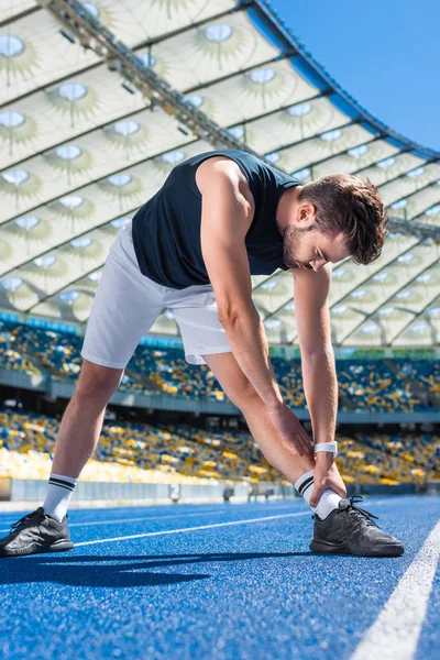 Jeune homme athlétique s'étirant sur la piste de course au stade de sport — Photo de stock