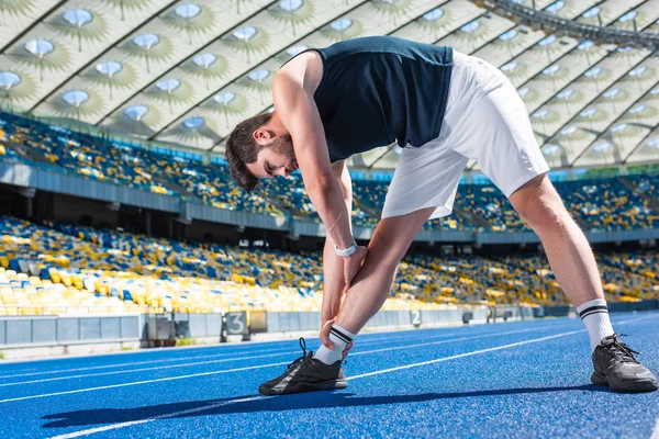 Bello giovane che si estende sulla pista da corsa allo stadio sportivo — Foto stock